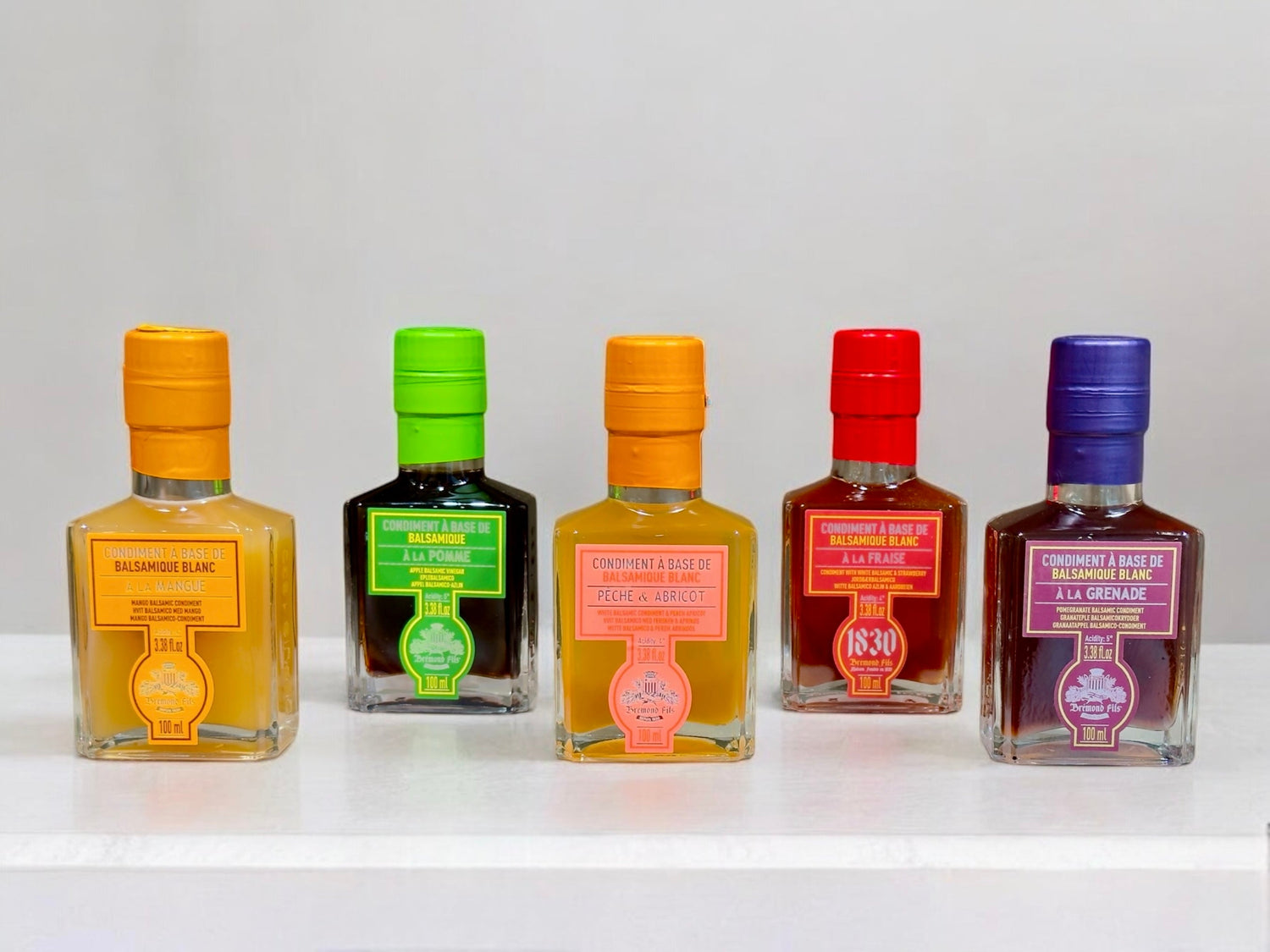 aison Bremond 1830 Balsamico Essig Condiment: Fünf Glasflaschen mit aromatisiertem Balsamico-Essig in den Sorten Mango, Apfel, Pfirsich-Aprikose, Erdbeere und Granatapfel. Farbige Etiketten und Verschlüsse heben die edlen Geschmacksrichtungen hervor.