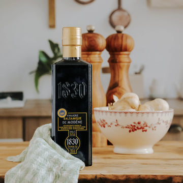 dle Flasche Aceto Balsamico Modena PGI mit goldener Kappe in einer gemütlichen Küche, umgeben von Gewürzmühlen, Knoblauch und rustikalem Dekor.