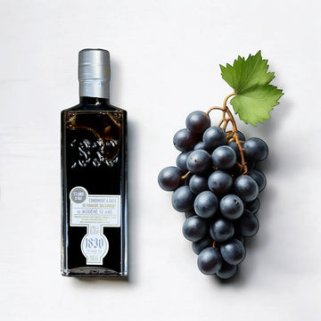 Hochwertiger 12 Jahre gereifter Balsamico Modena in einer eleganten Flasche, stehend neben dunklen Trauben. Perfekt für Feinschmecker und Gourmet-Küche.