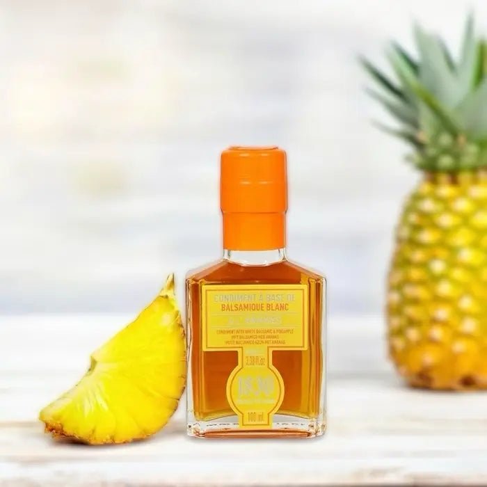 Flasche Ananas Essig Condiment mit leuchtend orangefarbenem Verschluss, dekoriert mit einer frischen Ananasscheibe und einer Ananas im Hintergrund. Perfekt für exotische Gerichte und kreative Rezeptideen.
