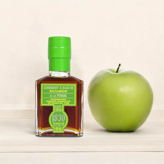 Flasche Apfel Balsamico Essig Condiment, 100 ml, mit grünem Verschluss neben einem frischen grünen Apfel auf hellem Hintergrund. Perfekt für vielseitige Gerichte. Jetzt Apfel Balsamico Essig Condiment kaufen und den fruchtigen Geschmack genießen.