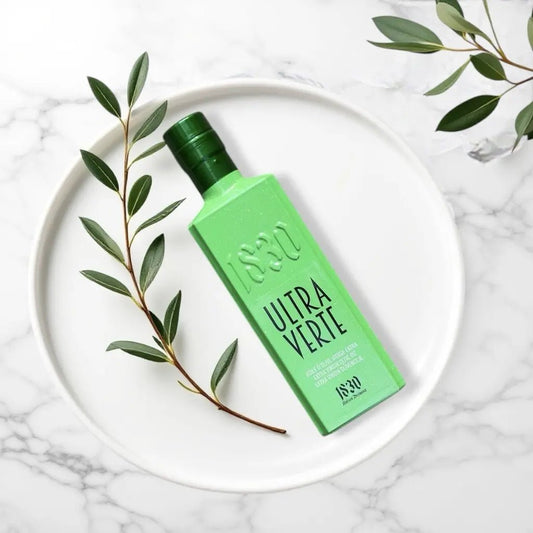 Premium Bio-Olivenöl aus Spanien – Ultra Verte in einer auffällig grünen Flasche, dekorativ auf einem weißen Teller mit Olivenzweig inszeniert