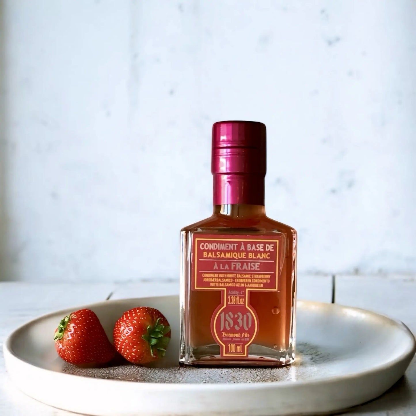 Flasche Erdbeer Balsamico Essig, 100 ml, mit glänzend rotem Verschluss, dekoriert mit frischen Erdbeeren auf einem eleganten Teller. Perfekt für kreative Gerichte und fruchtige Genussmomente.