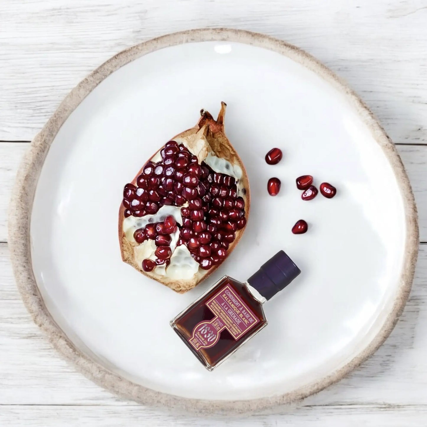 Maison Bremond 1830 Granatapfel-Balsamico-Essig mit aufgeschnittenem Granatapfel auf einem weißen Teller, dekoriert mit Granatapfelkernen