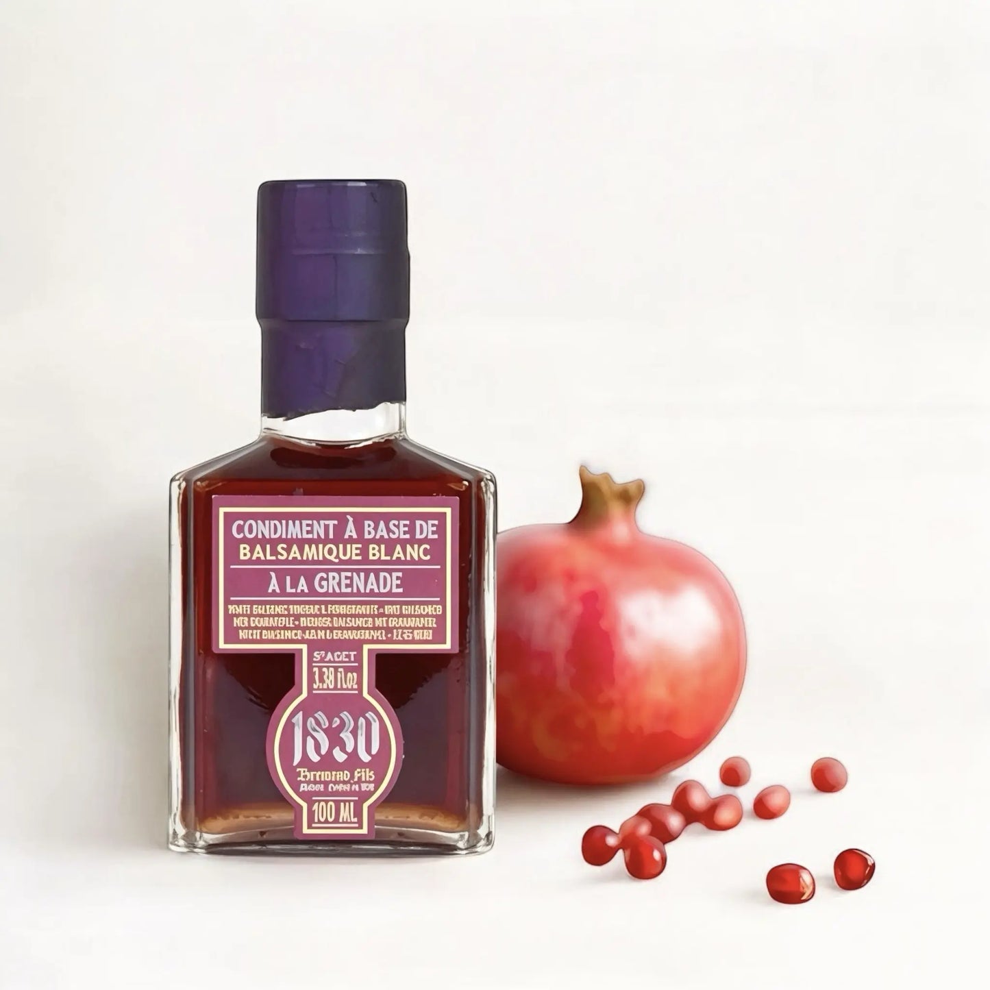 Eine elegante Glasflasche mit dunkelrotem Balsamico-Condiment auf Granatapfelbasis steht auf einer weißen Oberfläche. Die Flasche hat ein violett versiegeltes Oberteil und ein rechteckiges Etikett mit goldener und weißer Schrift auf rotem Hintergrund. Neben der Flasche liegt ein frischer Granatapfel mit glänzender roter Schale, aus dem einige Granatapfelkerne herausgerollt sind. Die Szene ist minimalistisch gestaltet und hebt die edle Optik des Produkts hervor.