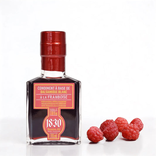 Edle Glasflasche mit Maison Brémond 1830 Himbeer-Balsamico-Condiment, verziert mit einem roten Etikett und passendem roten Verschluss. Daneben liegen frische Himbeeren, die die fruchtige Note des Essigs unterstreichen. Perfekt für Feinschmecker und Liebhaber hochwertiger Essigkreationen.