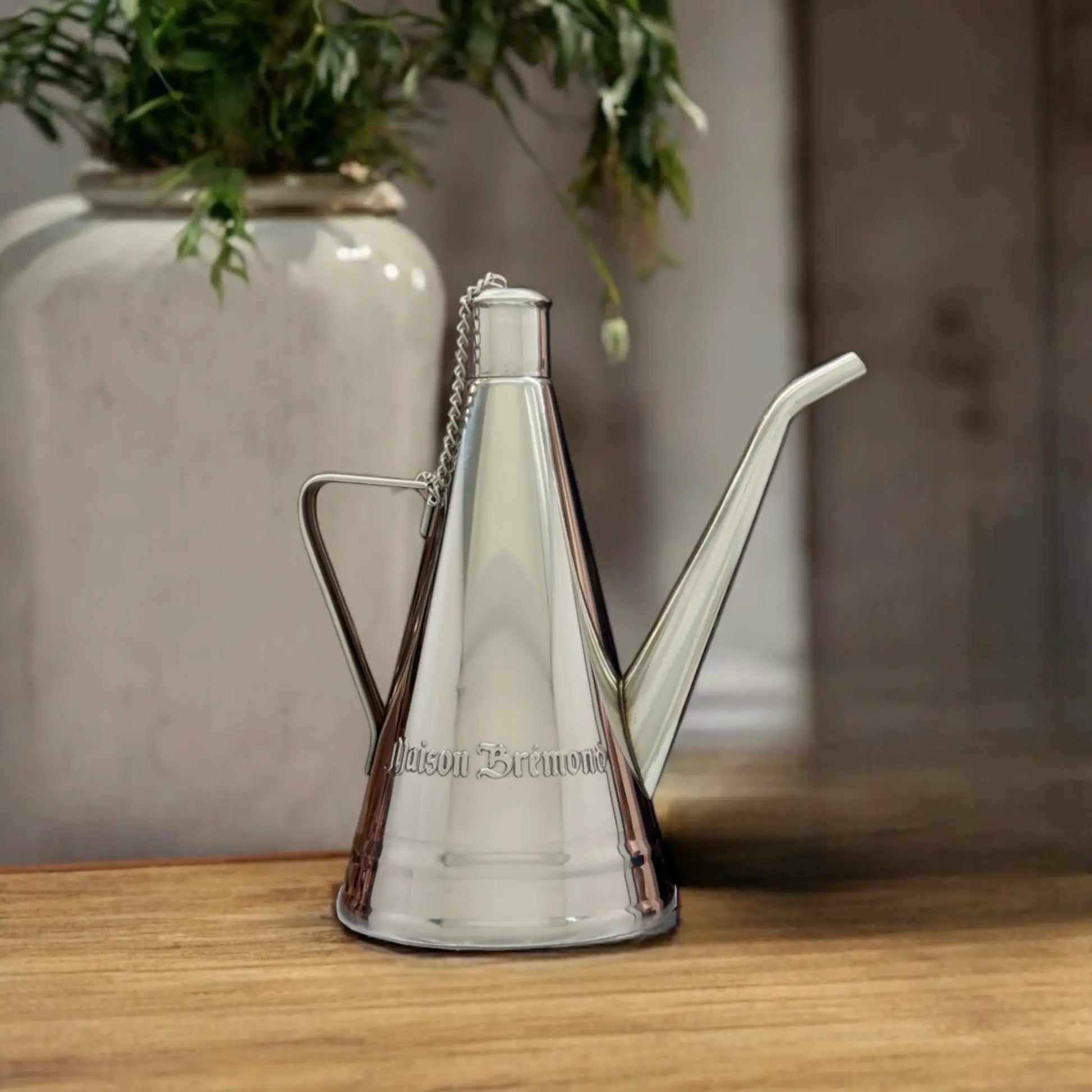 Maison Brémond Ölkanne für stilvolles Servieren – Hochwertige Edelstahl-Ölkanne mit langem Ausguss auf einem Holztisch, dekoriert mit Kräutern.