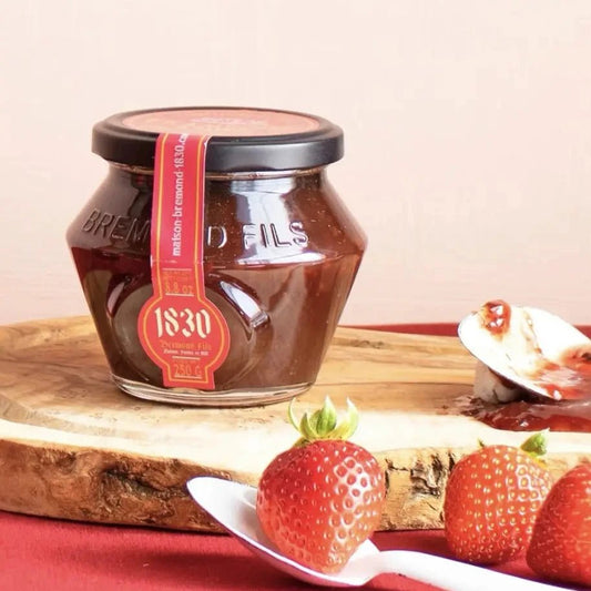 Erdbeer-Minze-Konfitüre im Glas mit rotem Etikett von Maison Brémond, dekoriert mit frischen Erdbeeren und Minzblättern auf einem Holzbrett.