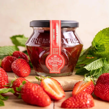 Erdbeer-Minze-Konfitüre im Glas mit rotem Etikett von Maison Brémond, dekoriert mit frischen Erdbeeren und Minzblättern auf einem Holzbrett.