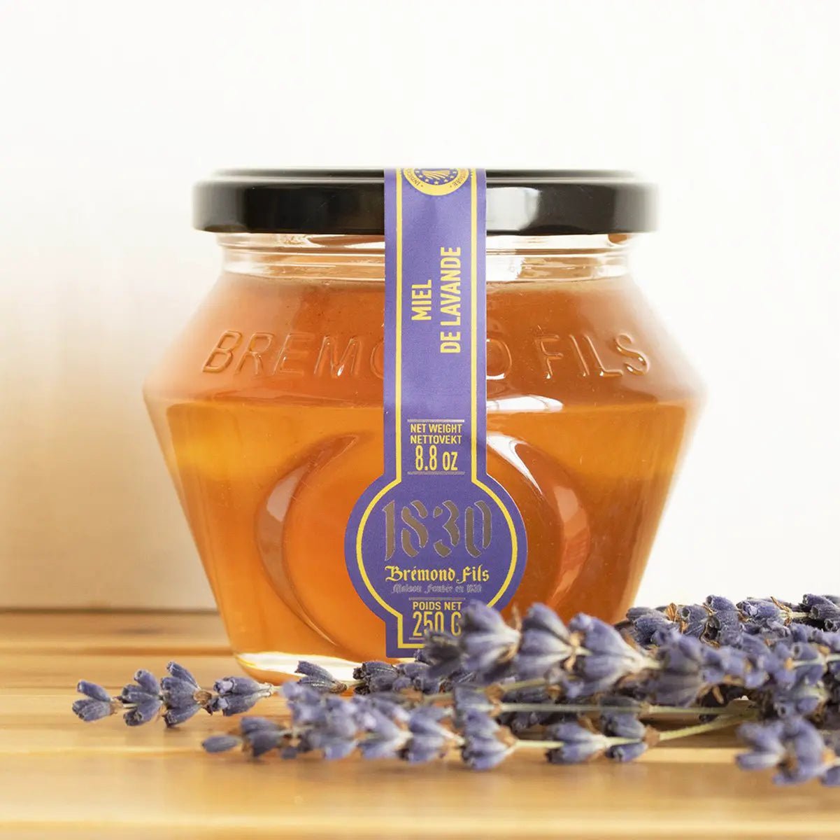 Ein Glas Lavendel Honig aus der Provence IGP, 250 g – cremiger Honig mit blumigem Geschmack aus den Lavendelfeldern der Provence. Vor Glas steht Lavendel Blüte