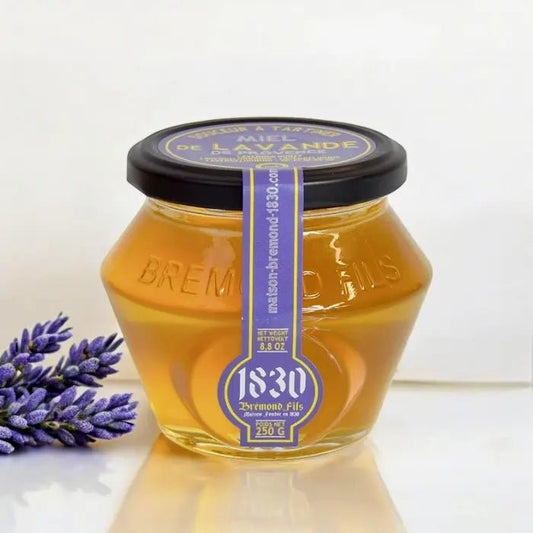 Ein Glas Lavendel Honig aus der Provence IGP, 250 g – cremiger Honig mit blumigem Geschmack aus den Lavendelfeldern der Provence. Vor Glas steht Lavendel Blüte