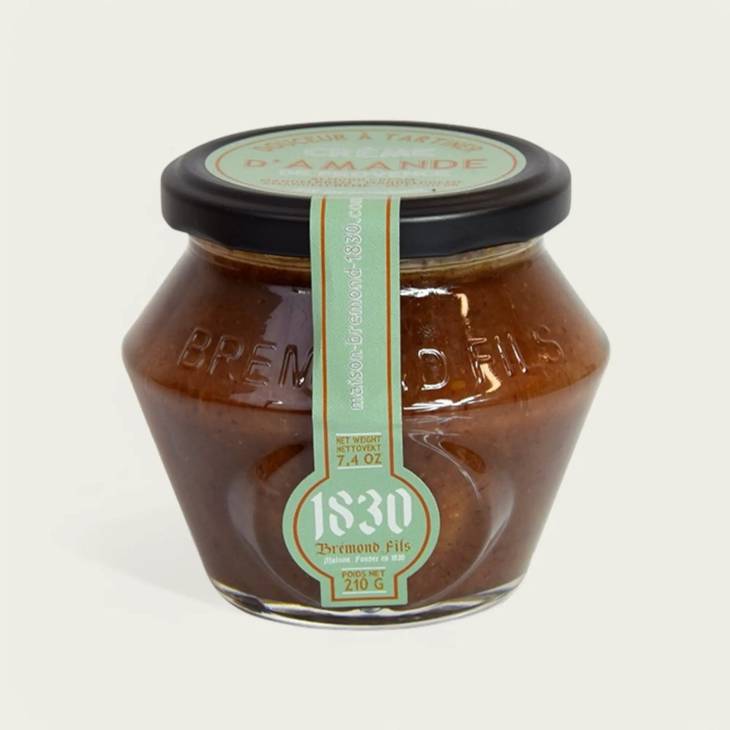 Sechseckiges Glas mit Mandel-Aufstrich von "Brémond Fils", 210 g. Das Glas hat einen schwarzen Deckel und ein pastellgrünes Etikett mit goldenen Details. Der Produktname sowie die Gewichtsangabe sind darauf zu sehen. Der Inhalt ist ein cremiger, brauner Aufstrich mit einer leicht glänzenden Oberfläche.