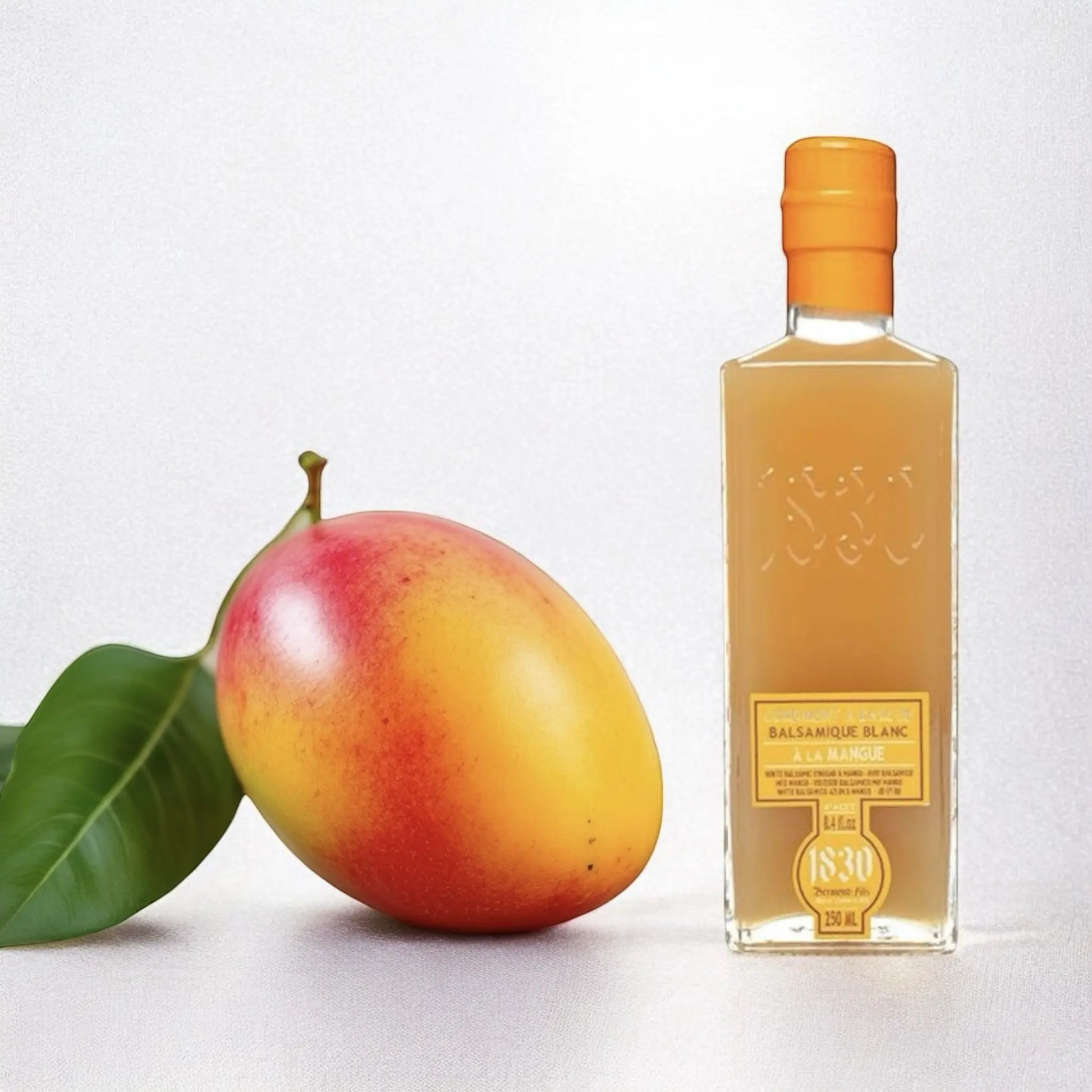 Glasflasche mit Mango-Balsamico-Essig neben einer frischen, reifen Mango