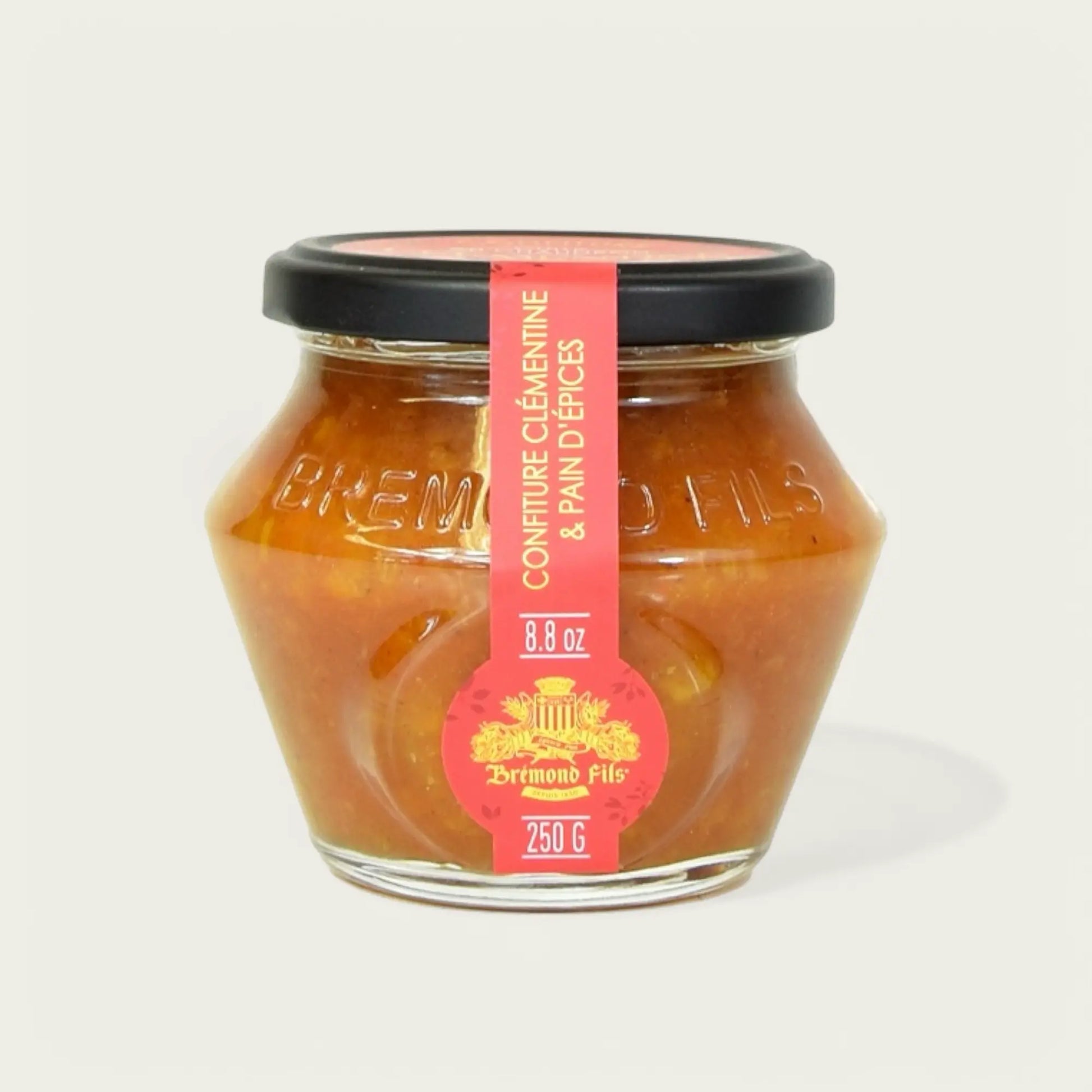 Glas mit Clementinen- und Lebkuchen-Konfitüre von "Brémond Fils", 250 g. Das sechseckige Glas hat einen schwarzen Deckel und ein rotes Etikett mit goldener Verzierung, auf dem der Produktname und die Gewichtsangabe zu sehen sind. Der Inhalt ist eine gold-orangefarbene Marmelade mit sichtbaren Fruchtstückchen.