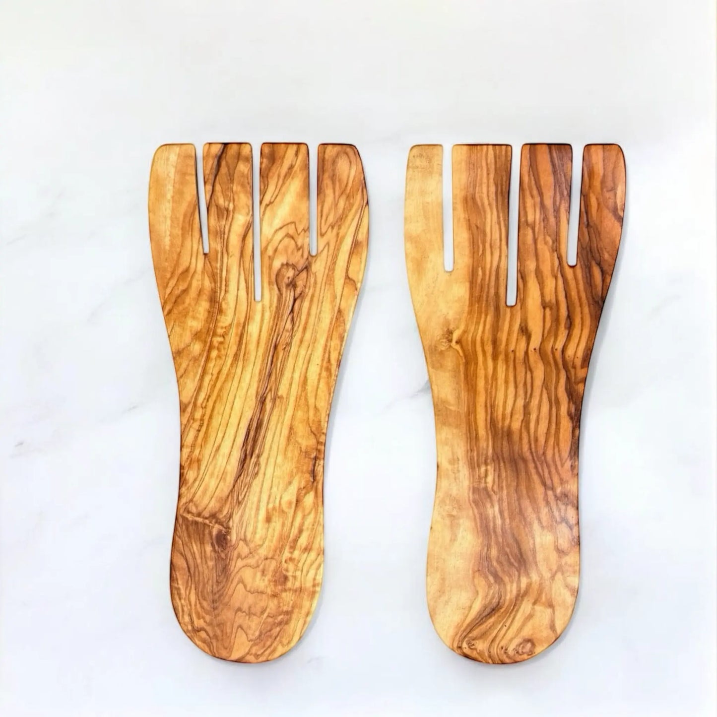 Salathände aus Olivenholz mit natürlicher Maserung und geschwungenen Zinken, nebeneinander auf hellem Hintergrund liegend. Ideal als hochwertiges Salatbesteck für stilvolles Servieren.