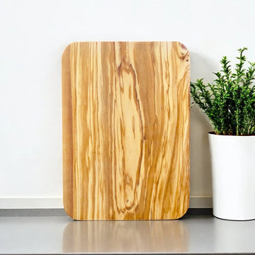 Ein rechteckiges Schneidebrett aus Olivenholz mit einer markanten Maserung, das auf einer hellen Oberfläche liegt.