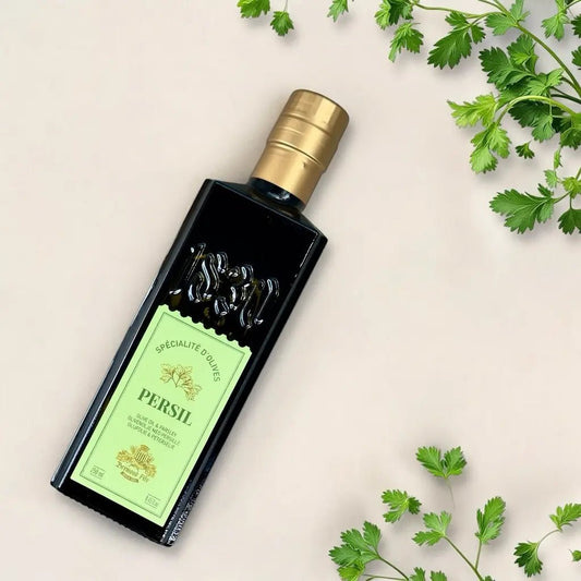 Maison Brémond 1830 Olivenöl mit Petersilie – Flasche liegend umgeben von frischen Petersilienblättern auf beigem Hintergrund