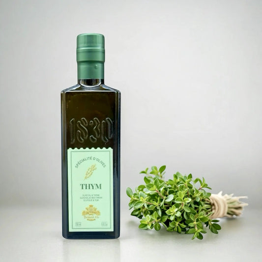 Flasche Olivenöl mit Thymian von Maison Brémond 1830 aus Frankreich, stehend neben einem frischen Bund Thymian auf hellem Hintergrund