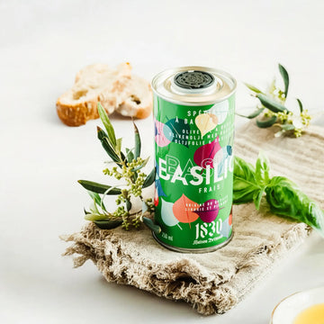 Maison Brémond Olivenöl mit Basilikum 250 ml – Stilvolle Dose mit frischem Basilikumaroma, modern inszeniert mit Olivenzweigen und rustikalem Leinentuch.