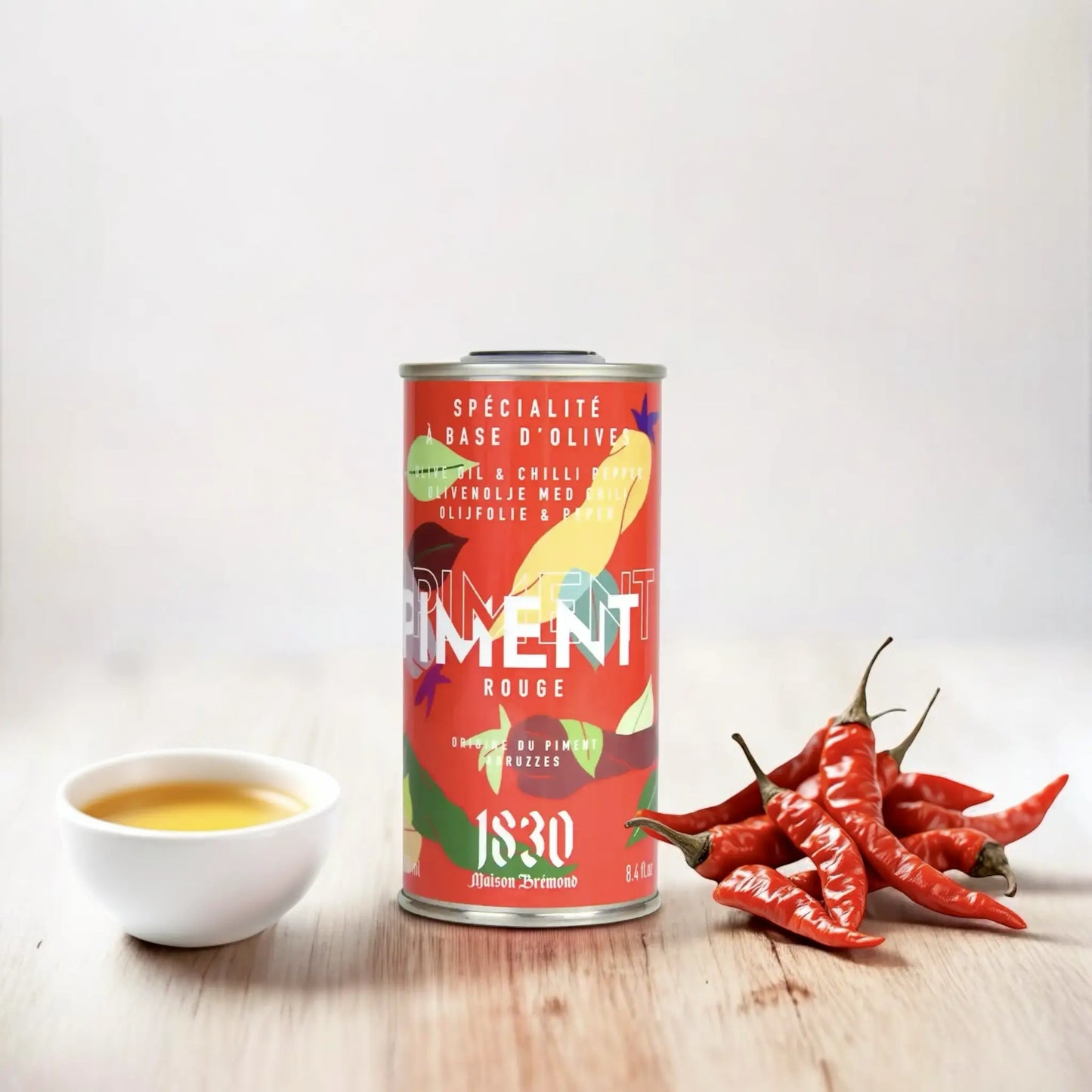 Maison Brémond Olivenöl mit Chili und frischen Schoten – Hochwertiges, würziges Olivenöl neben roten Chilischoten und einer Schale Olivenöl auf weißem Hintergrund.