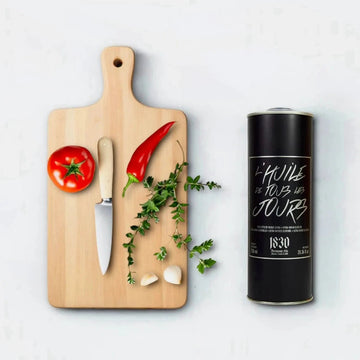 Testsieger Olivenöl zum Braten, Kochen & Backen aus Griechenland – hochwertiger schwarzer Kanister von Maison Brémond 1830 mit frischen Zutaten auf Holzbrett.