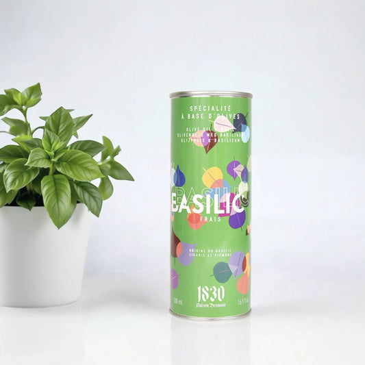 Maison Brémond Olivenöl mit Basilikum 500 ml – Aromatisiertes Olivenöl in einer grünen Dose mit buntem Design, neben einer frischen Basilikumpflanze.