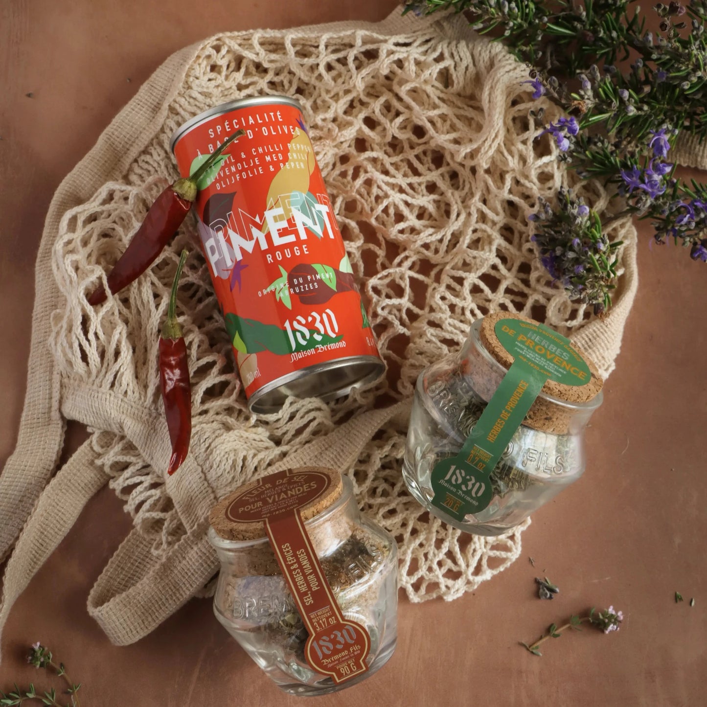 Maison Brémond Chili-Olivenöl mit Gewürzen – Aromatisiertes Olivenöl, begleitet von Provence-Kräutern und Gewürzmischungen in einer rustikalen Netztasche.