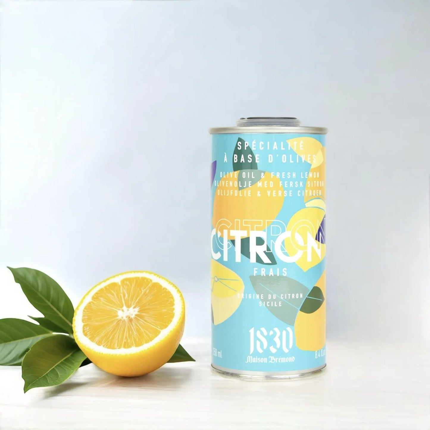 Design-Dose Olivenöl mit 15 % frischen Zitronen von Maison Brémond 1830, daneben eine aufgeschnittene Zitrone mit Blättern. Extra natives Olivenöl mit natürlichem Zitronenaroma, ideal für Salate, Fisch und mediterrane Speisen. Jetzt kaufen.