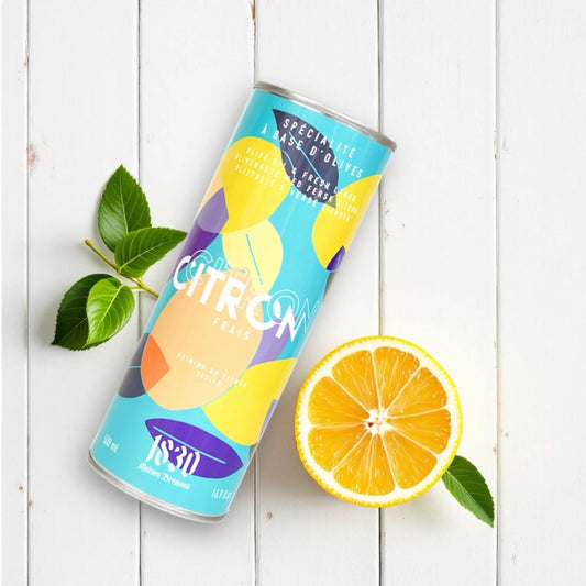 Design-Dose Olivenöl mit 15 % frischen Zitronen von Maison Brémond 1830, liegend auf einem weißen Holzhintergrund. Daneben eine aufgeschnittene Zitrone mit Blättern. Extra natives Olivenöl mit natürlichem Zitronenaroma, ideal für Salate, Fisch und mediterrane Gerichte. Jetzt kaufen.