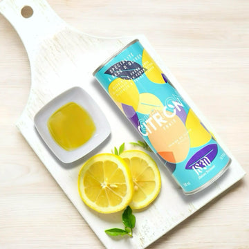 Design-Dose Olivenöl mit 15 % frischen Zitronen von Maison Brémond 1830 auf einem weißen Holzbrett. Daneben eine Schale mit Olivenöl und frische Zitronenscheiben. Extra natives Olivenöl mit natürlichem Zitronenaroma, ideal für Salate, Fisch und mediterrane Gerichte. Jetzt kaufen.