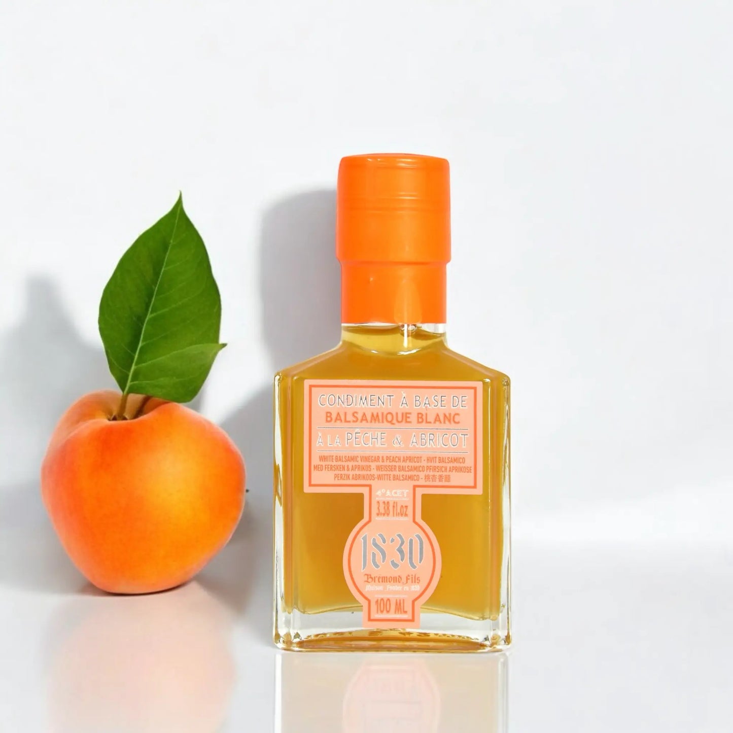 Flasche weißer Balsamico Essig mit Pfirsich und Aprikose, 100 ml, mit leuchtend orangefarbenem Verschluss, dekoriert mit einer frischen Aprikose und Blatt. Perfekt für fruchtige Gerichte und kreative Rezepte.
