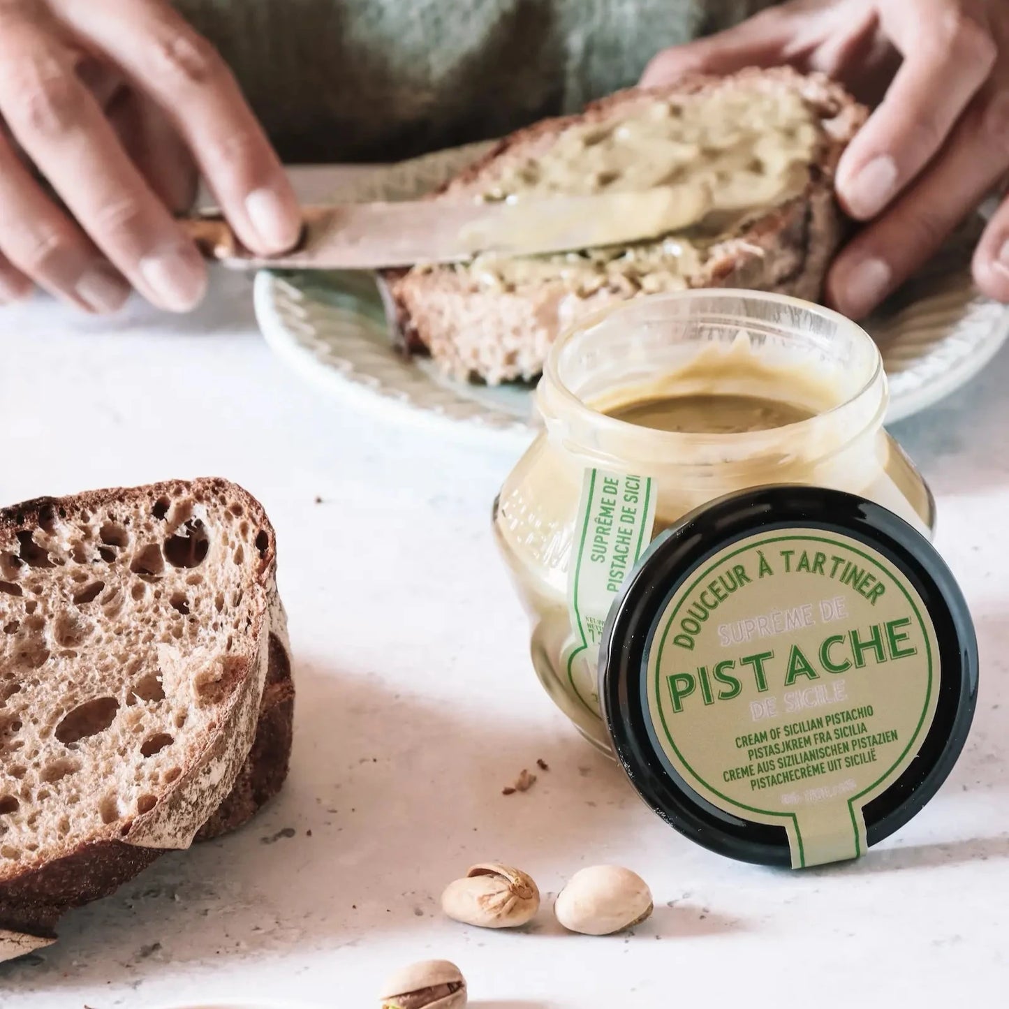 Glas mit sizilianischer Pistaziencreme auf einem Tisch, daneben geröstetes Brot mit Pistaziencreme bestrichen.