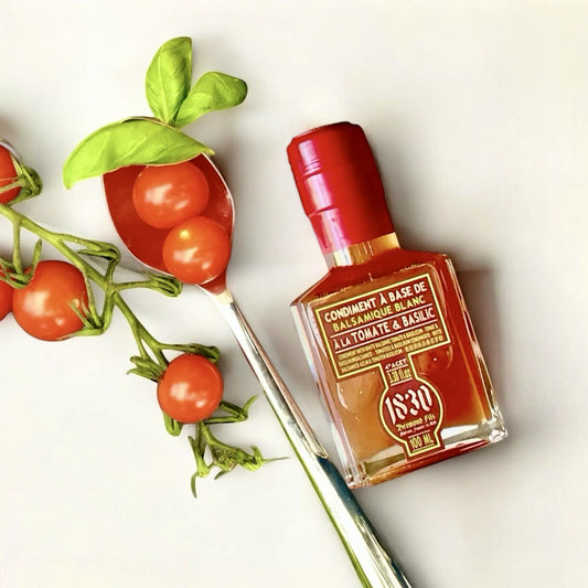 Flasche Tomaten Basilikum Balsamico Essig, 100 ml, mit glänzend rotem Verschluss, dekoriert mit frischen Cherrytomaten, Basilikum und einem Löffel. Perfekt für mediterrane Gerichte und kreative Rezepte.