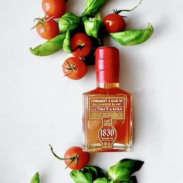Flasche Tomaten Basilikum Balsamico Essig, 100 ml, mit rotem Verschluss, umgeben von frischen Cherrytomaten und Basilikumblättern. Ideal für mediterrane Gerichte und kreative Rezepte.