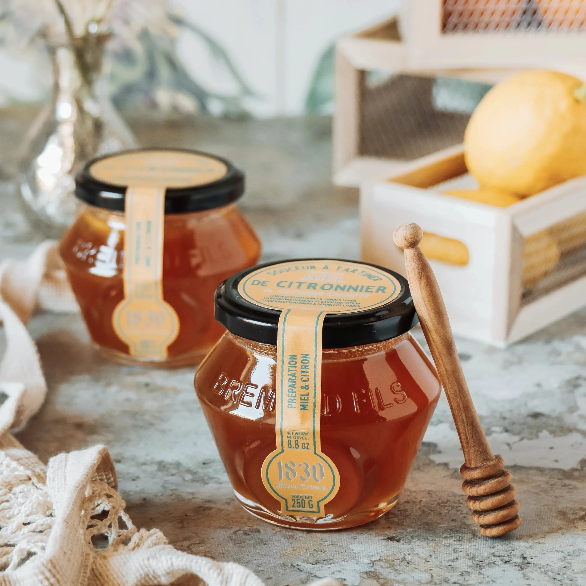 Zitronenblütenhonig mit kandierter Zitrone im Glas – Maison Brémond 1830, 250 g, mit Honiglöffel und Zitrone im Hintergrund