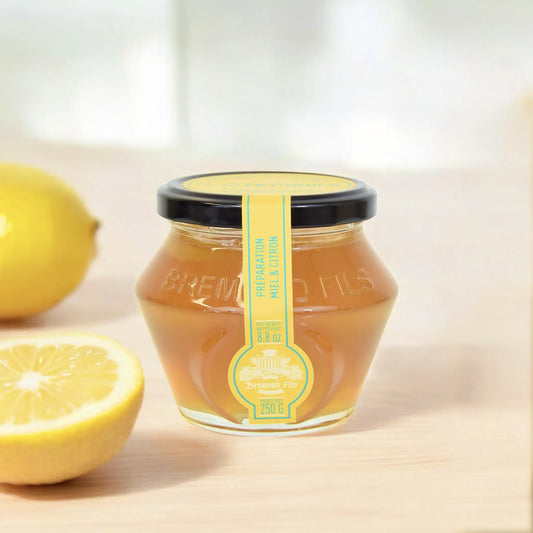 Zitronenblütenhonig im Glas von Maison Brémond 1830 – 250 g, vor frischer Zitrone auf hellem Hintergrund