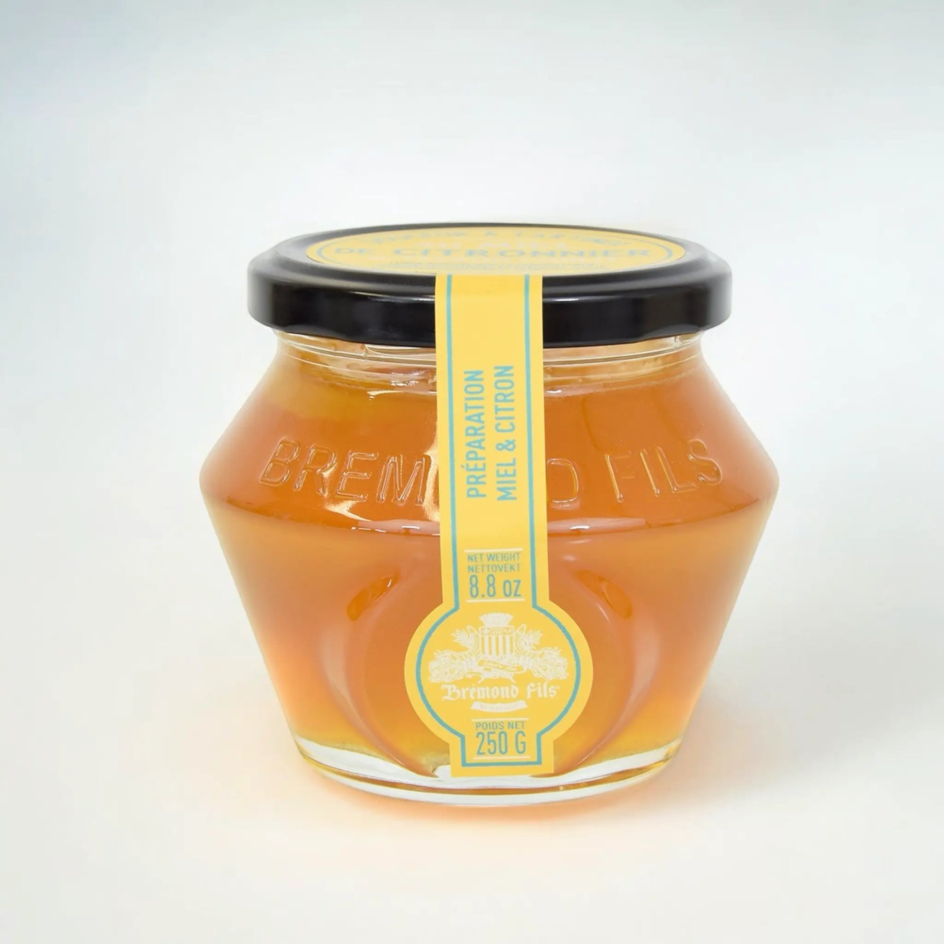 Zitronenblütenhonig im Glas von Maison Brémond 1830 – 250 g, vor frischer Zitrone auf hellem Hintergrund