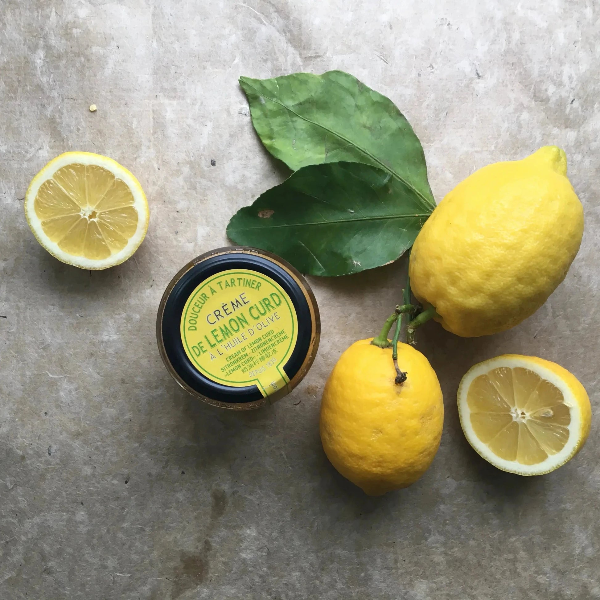 Maison Brémond Zitronencreme (Lemon Curd) im Glas, umgeben von frischen Zitronen mit Blättern – fruchtig, cremig und ideal für Brot & Desserts.