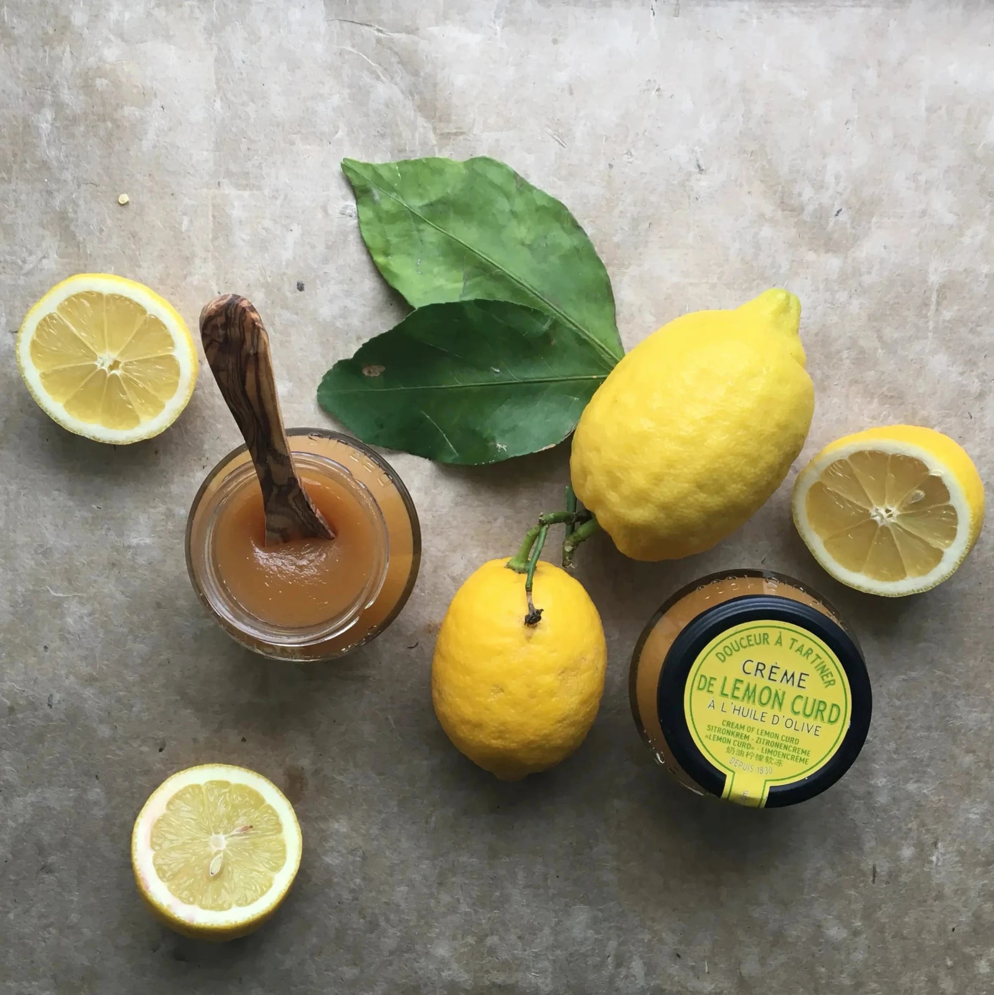 Maison Brémond Zitronencreme (Lemon Curd) im offenen Glas mit Holzlöffel, umgeben von frischen Zitronen – cremig, fruchtig und perfekt für Brot & Desserts.