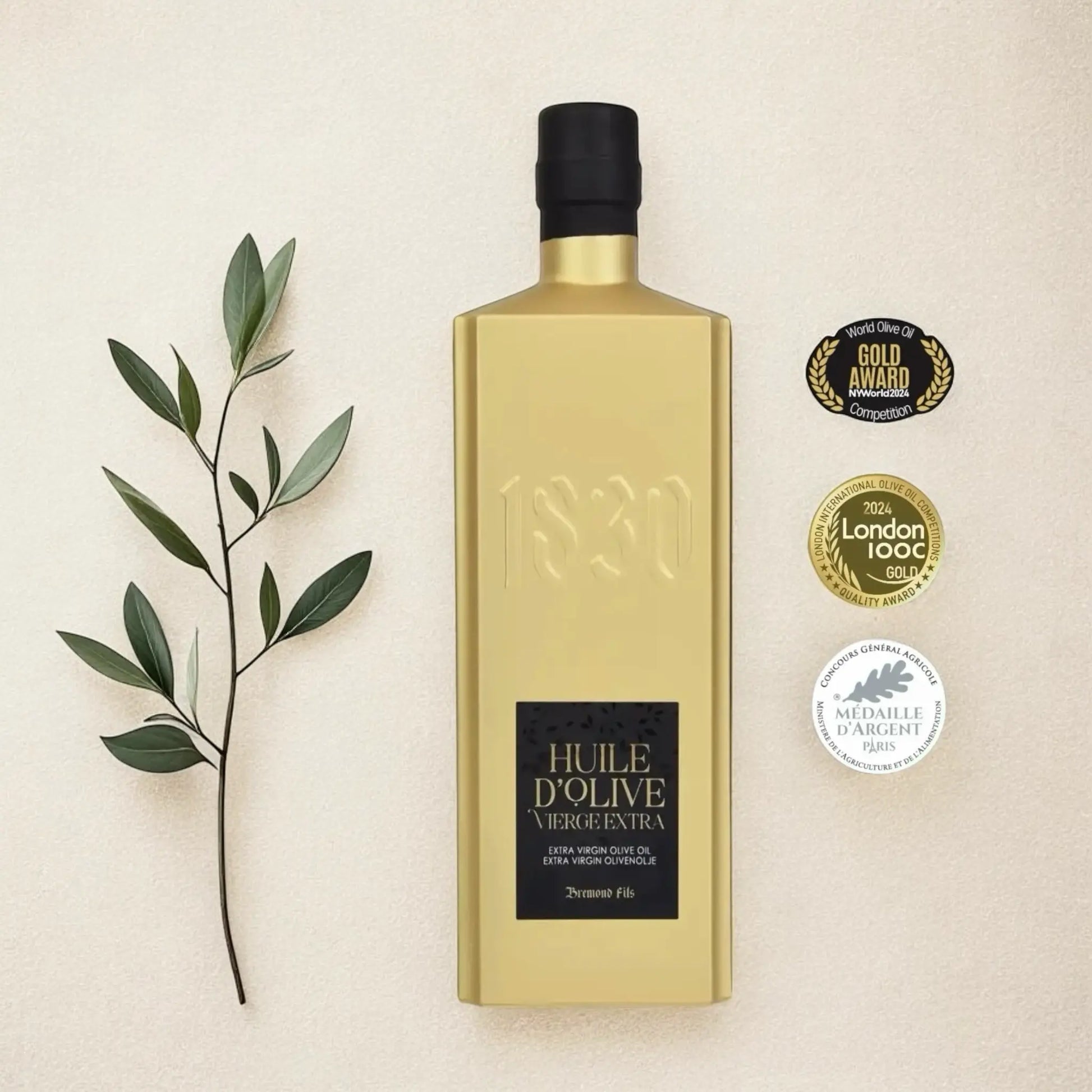 Goldene Flasche mit preisgekröntem Bio-Olivenöl aus Frankreich neben Oliven Zweig – ausgezeichnet mit internationalen Gold- und Silbermedaillen, ein Symbol für Qualität und Exzellenz.