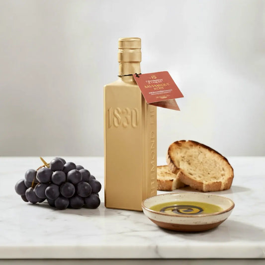 15 Jahre gereifter Aceto Balsamico di Modena in goldener 1830-Flasche – Premium Essig aus Italien, serviert mit Olivenöl, Brot und Trauben.
