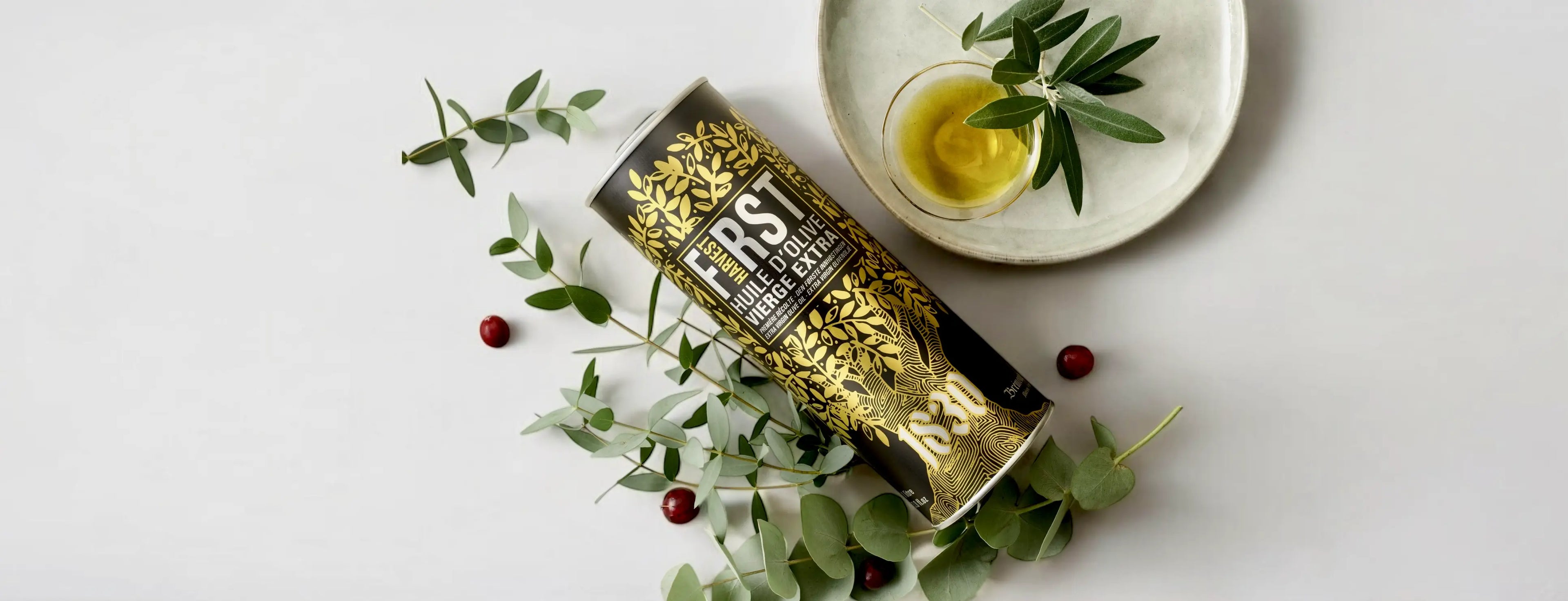  Eine edle schwarze Dose Bio Olivenöl mit goldener Verzierung aus der neuen Ernte, stilvoll arrangiert mit frischen Olivenzweigen, einer Schale Olivenöl und roten Beeren auf hellem Hintergrund. Perfekt für Feinschmecker, die hochwertiges Bio Olivenöl kaufen und genießen möchten.