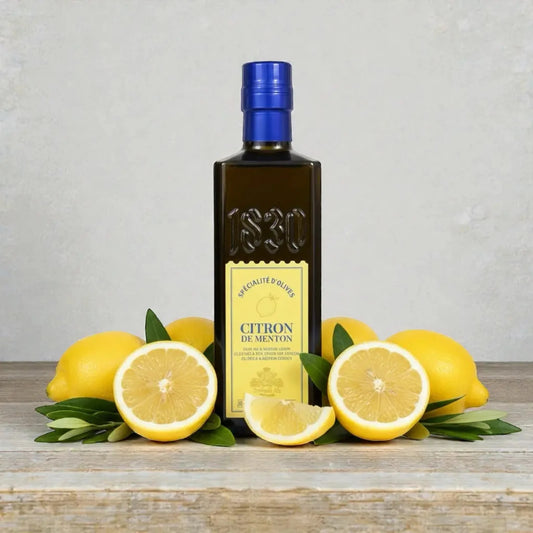 Maison Brémond 1830 Zitronen-Olivenöl aus Menton, umgeben von frischen Zitronen auf rustikalem Holztisch – aromatisches Olivenöl mit natürlichem Zitronenaroma.