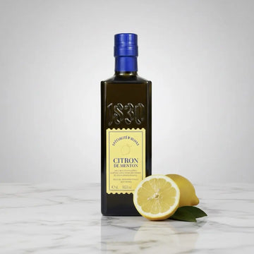 Flasche Maison Brémond 1830 Zitronen-Olivenöl auf Holztisch in heller Küche mit frischer Zitrone – feines Olivenöl veredelt mit Menton-Zitronen.