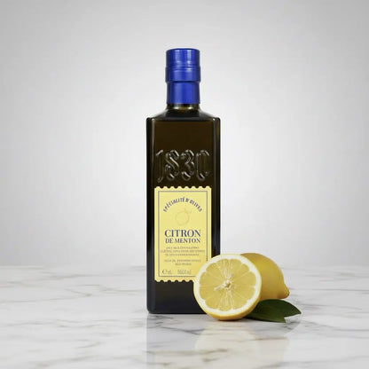Flasche Maison Brémond 1830 Zitronen-Olivenöl auf Holztisch in heller Küche mit frischer Zitrone – feines Olivenöl veredelt mit Menton-Zitronen.