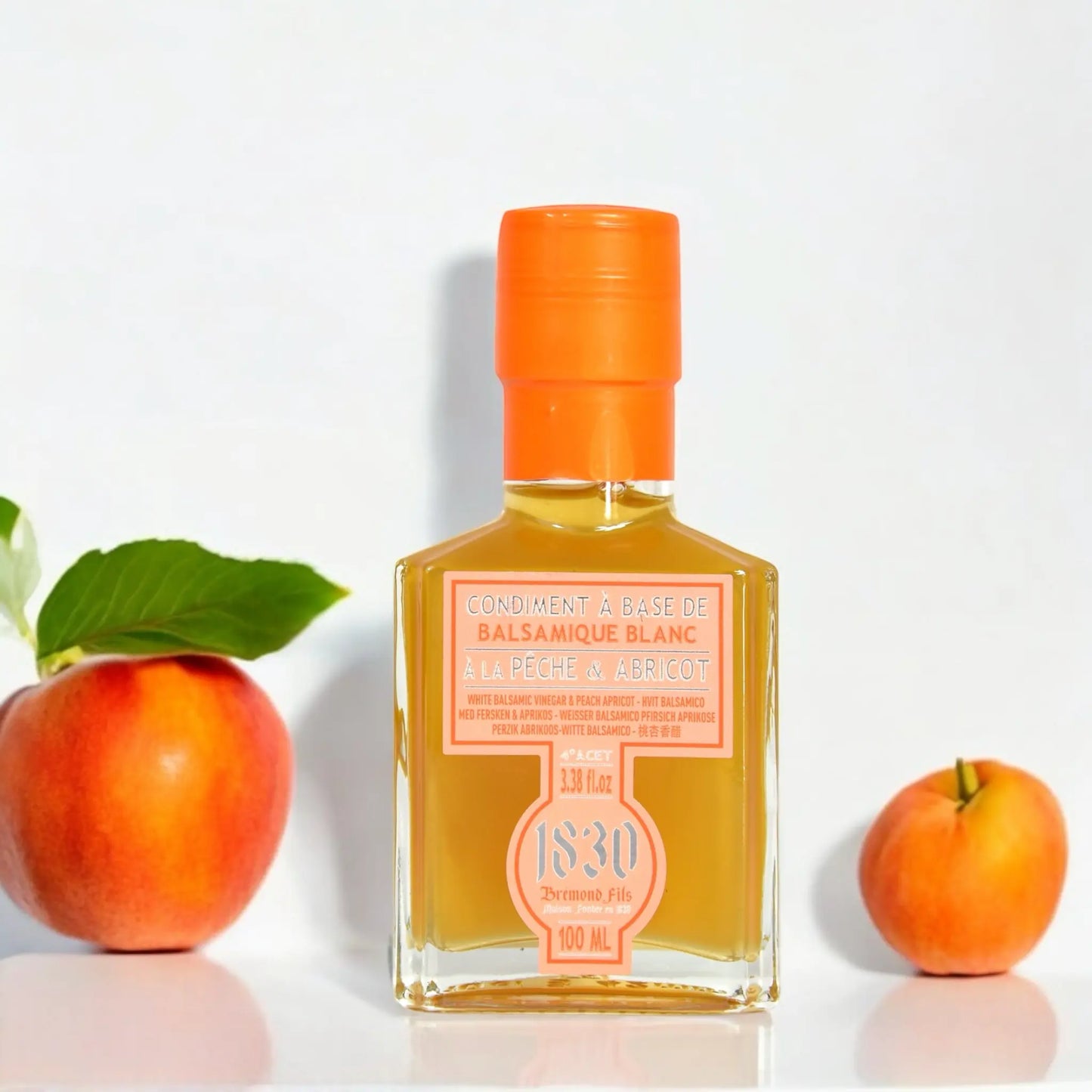 Flasche weißer Balsamico Essig mit Pfirsich und Aprikose, 100 ml, dekoriert mit frischen Früchten und leuchtend orangefarbenem Verschluss. Perfekt für fruchtige und kreative Gerichte.
