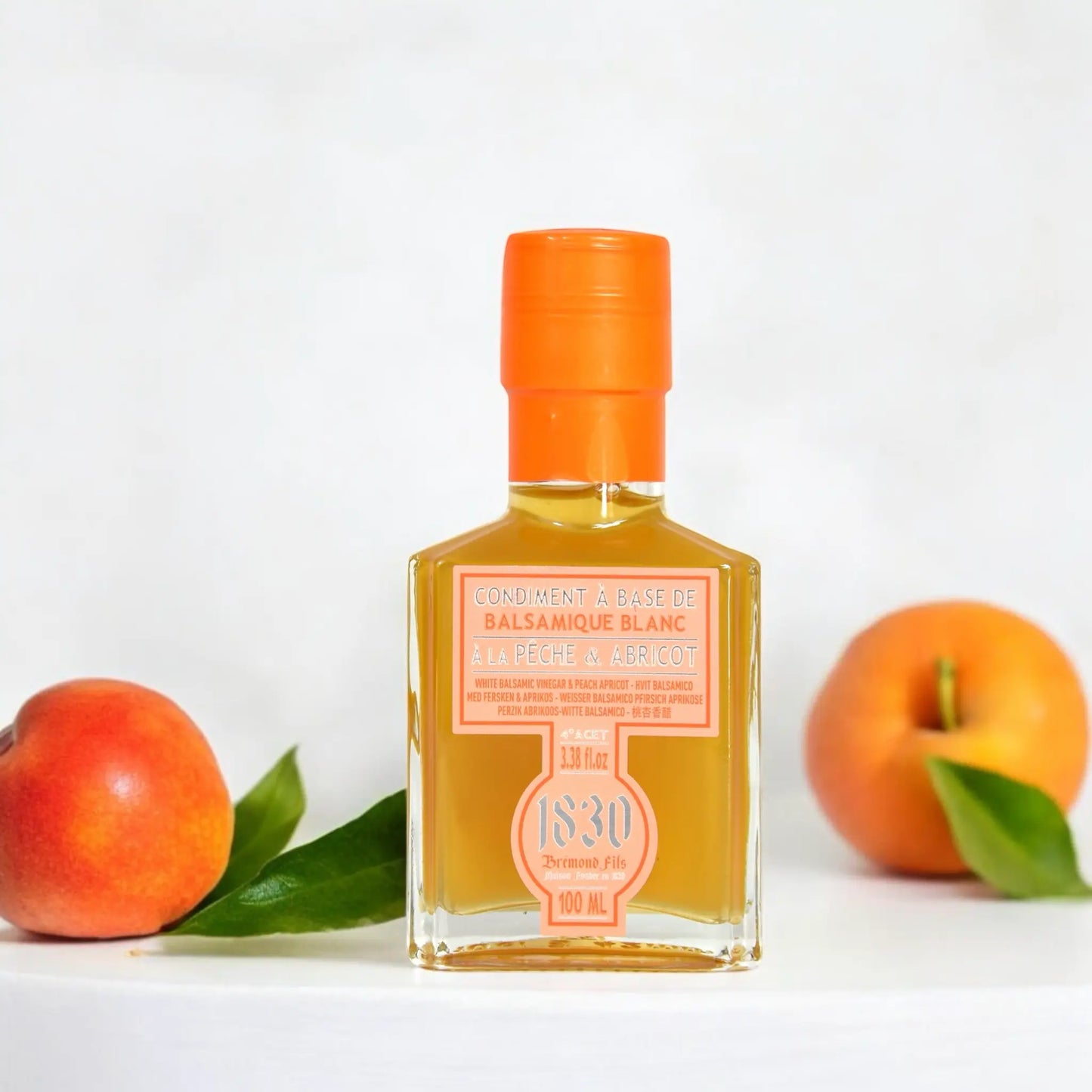 Edle Flasche weißer Balsamico Essig mit Pfirsich und Aprikose von Maison Brémond 1830, dekoriert mit frischen Früchten im Hintergrund. Perfekt für kreative Gerichte und fruchtige Aromen.