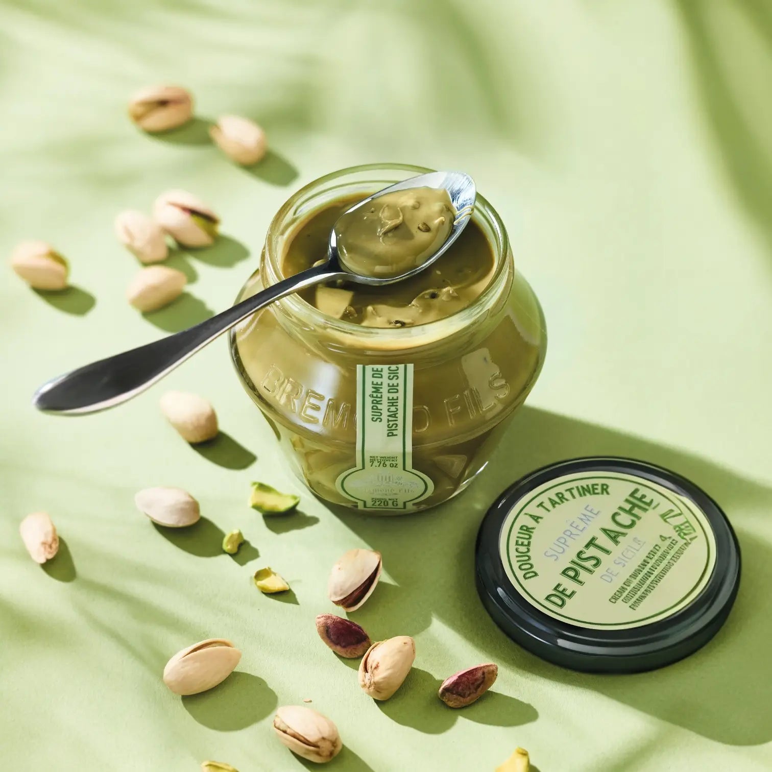 Pistaziencreme-Glas mit einem Löffel Pistaziencreme, dekorativ arrangiert auf grünem Hintergrund mit Pistazien.
