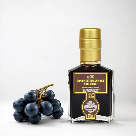 Exklusiver schwarzer Balsamico-Essig – 30 Jahre in einer eleganten Flasche mit goldener Kappe, begleitet von dunklen Trauben.
