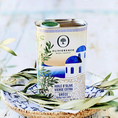 500 ml Dose griechisches Olivenöl von Oliviers & Co, stilvoll präsentiert auf einem rustikalen Teller mit Olivenzweigen. Die Verpackung zeigt eine traditionelle blau-weiße Kapelle und betont die hohe Qualität des extra nativen Olivenöls aus Griechenland. Ideal zum Kaufen für authentische mediterrane Küche.